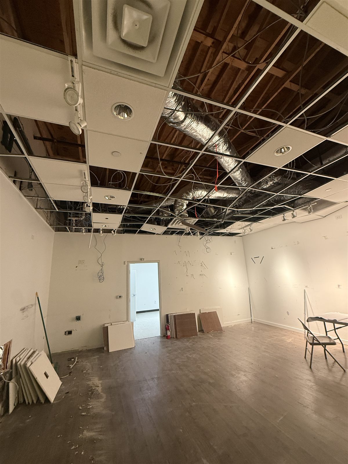 Demo phase of the L'Occitane space — previous tenant's ceiling grid opened with ductwork and wiring exposed