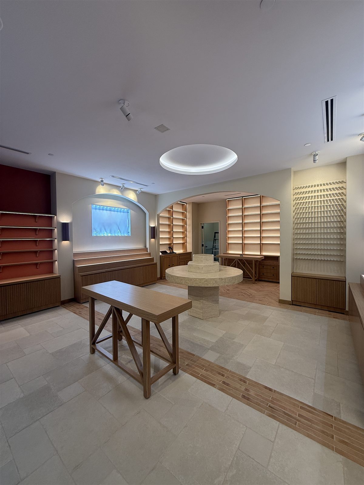 Finished L'Occitane interior with arched display niches, travertine centerpiece, and linear slot diffusers integrated into the ceiling