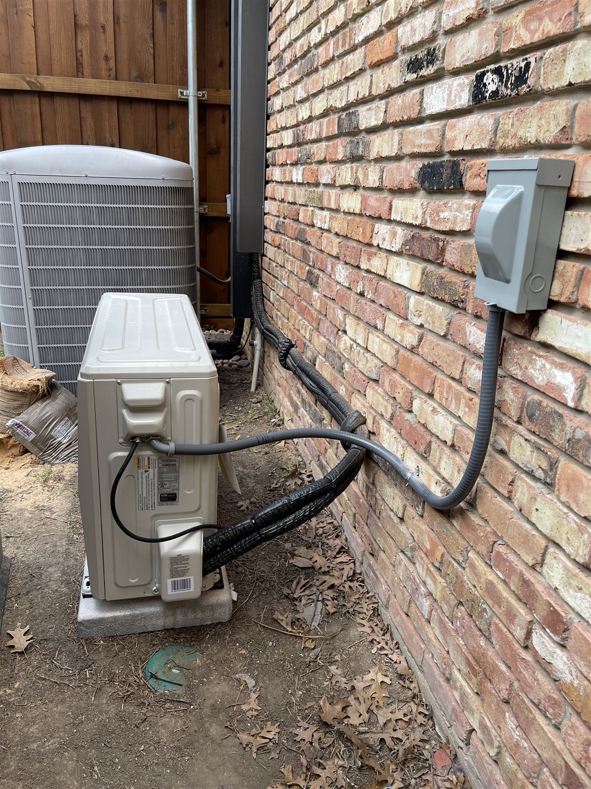 New outdoor HVAC units with insulated line sets and weatherproof disconnect installed at a brick DFW home